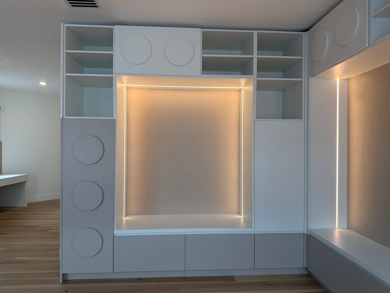 White built-in LED-lit niche flanked by circular disc-pull cabinet doors