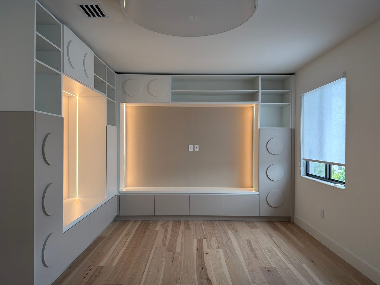 White built-in wall unit with circular pulls and LED niche from a different angle, window visible
