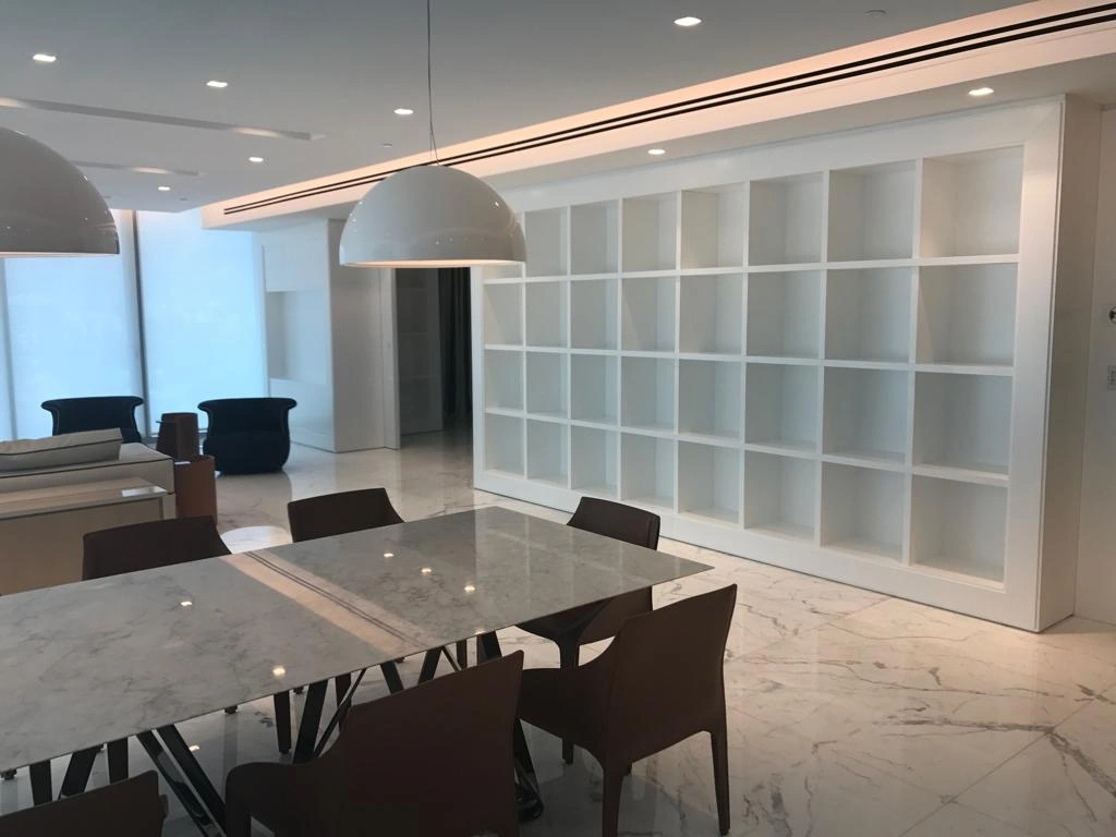 White grid-pattern bookshelf spanning a wall behind a dining table with veined stone top and dark chairs