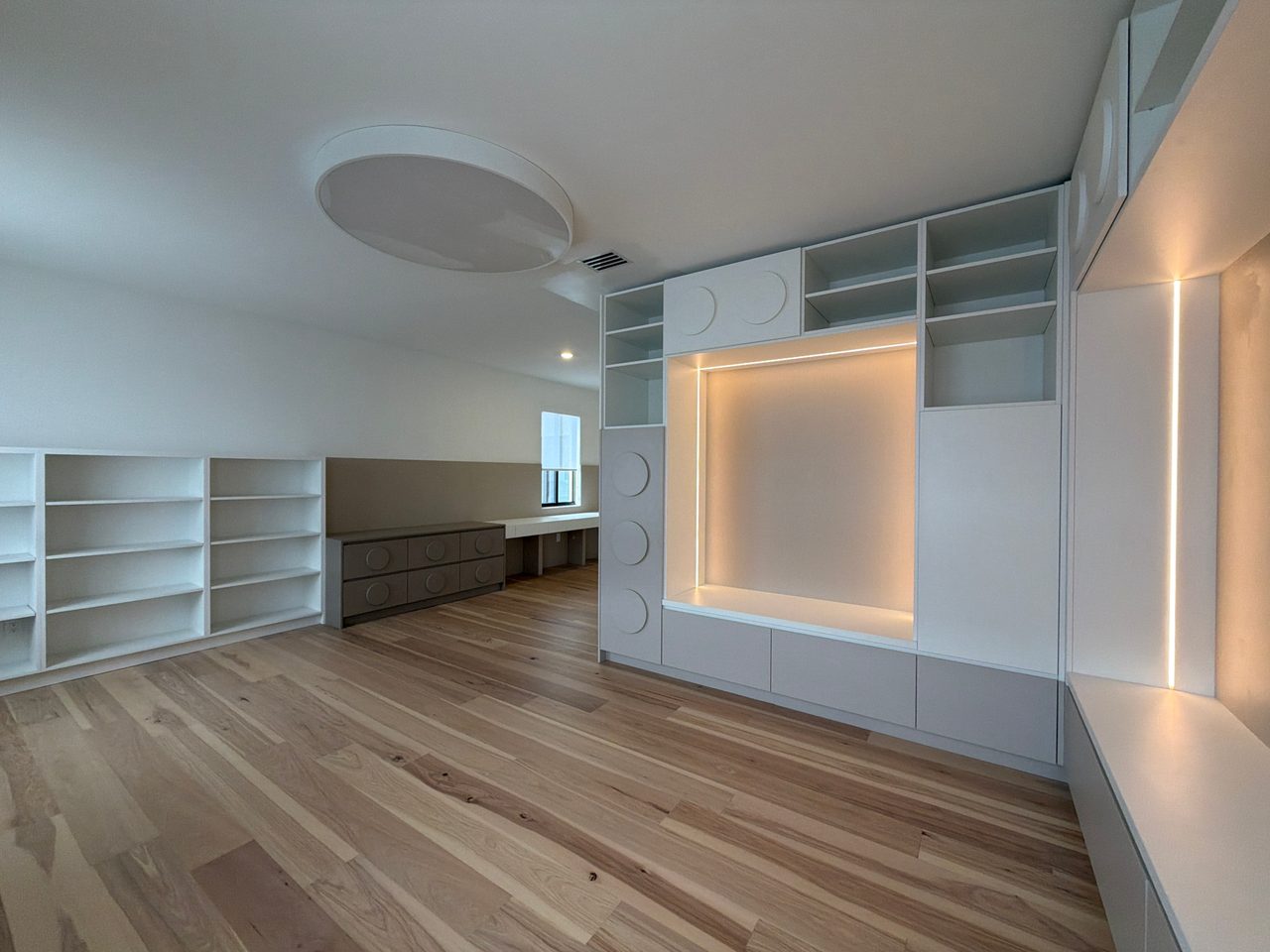 Empty room with white open shelving units on both sides and a beige built-in dresser/desk visible in the background