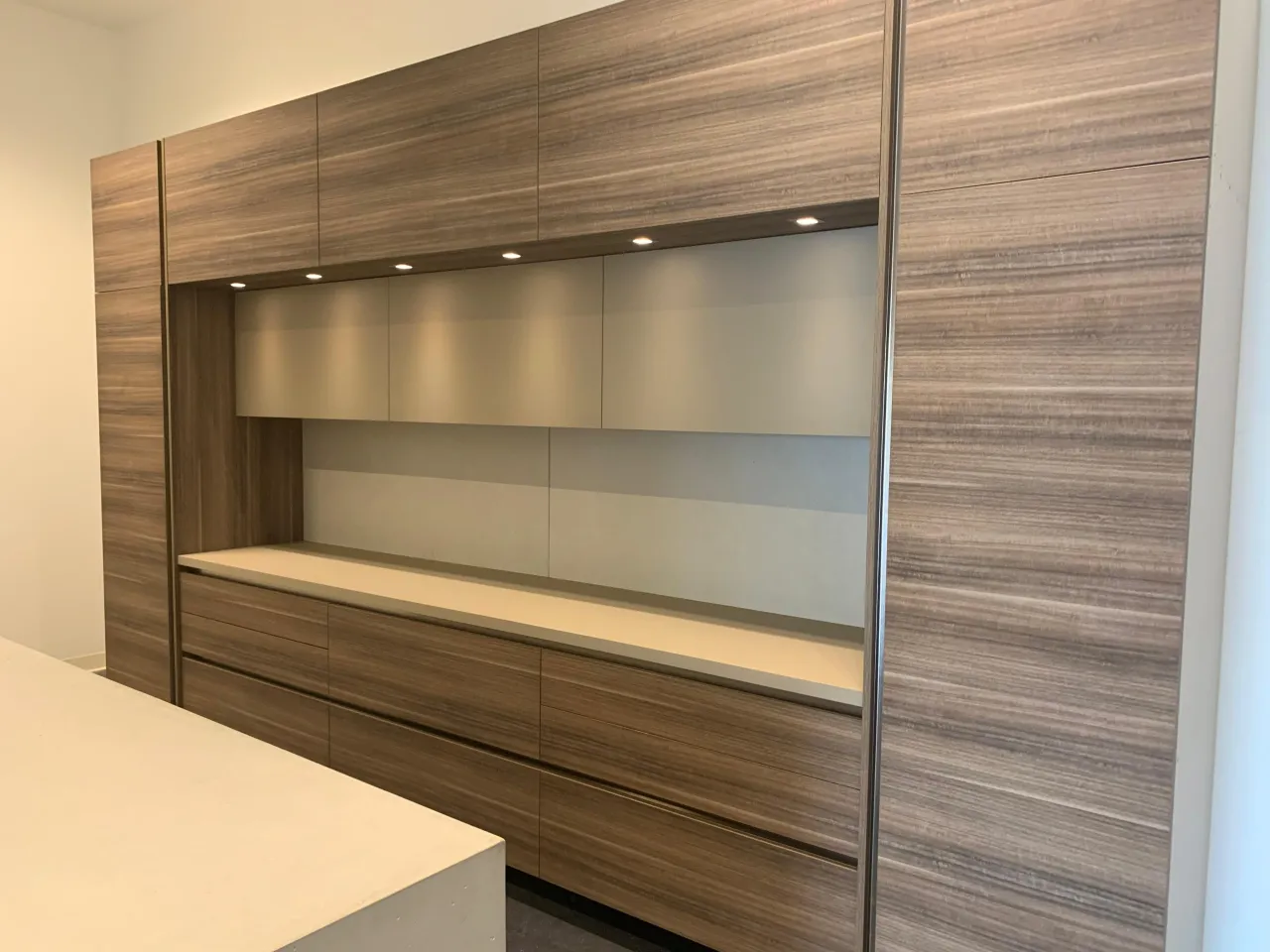 Wood-grain wall unit with three frosted gray upper doors, a pale counter with drawer bank below, and full-height panels at each side