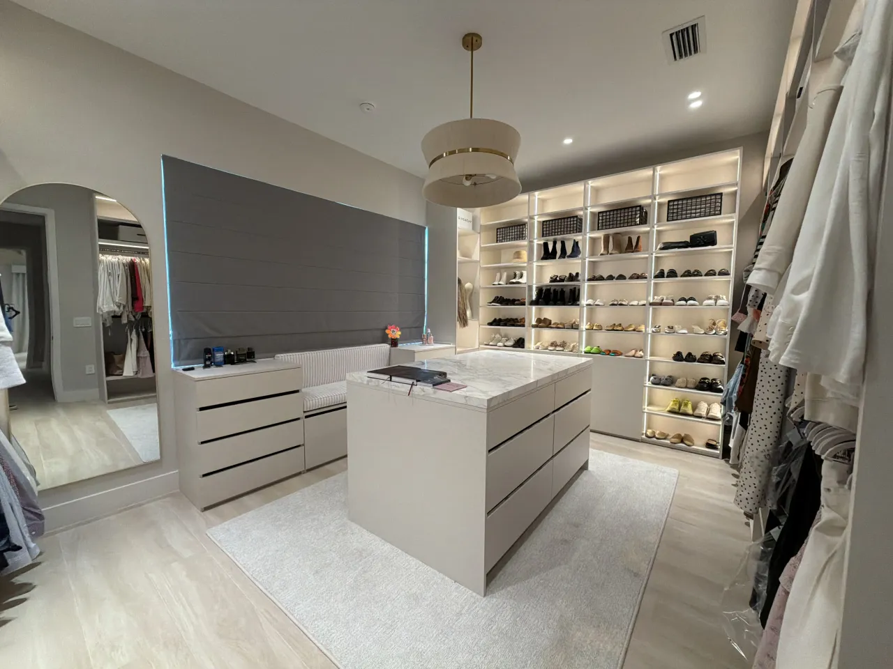 Closet with an arched mirrored doorway, a dresser, a stone island, and a shoe/handbag wall