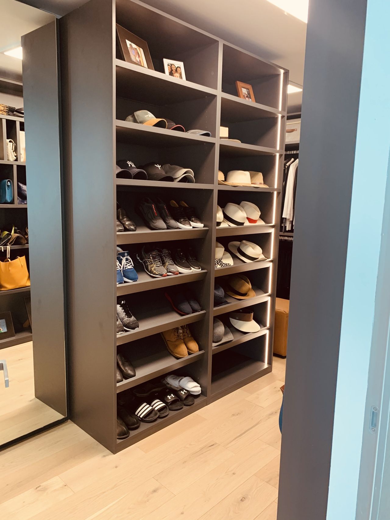 Charcoal open shelving holding shoes, hats and framed photos, a mirrored panel at left and hanging clothes beyond, light wood floor