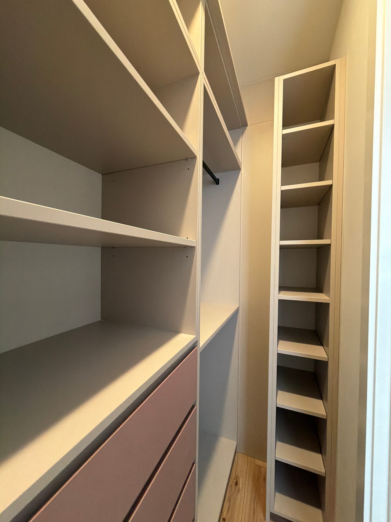 Close view of cream closet shelving with a tall narrow cubby column at right and mauve-pink drawer fronts below the shelves