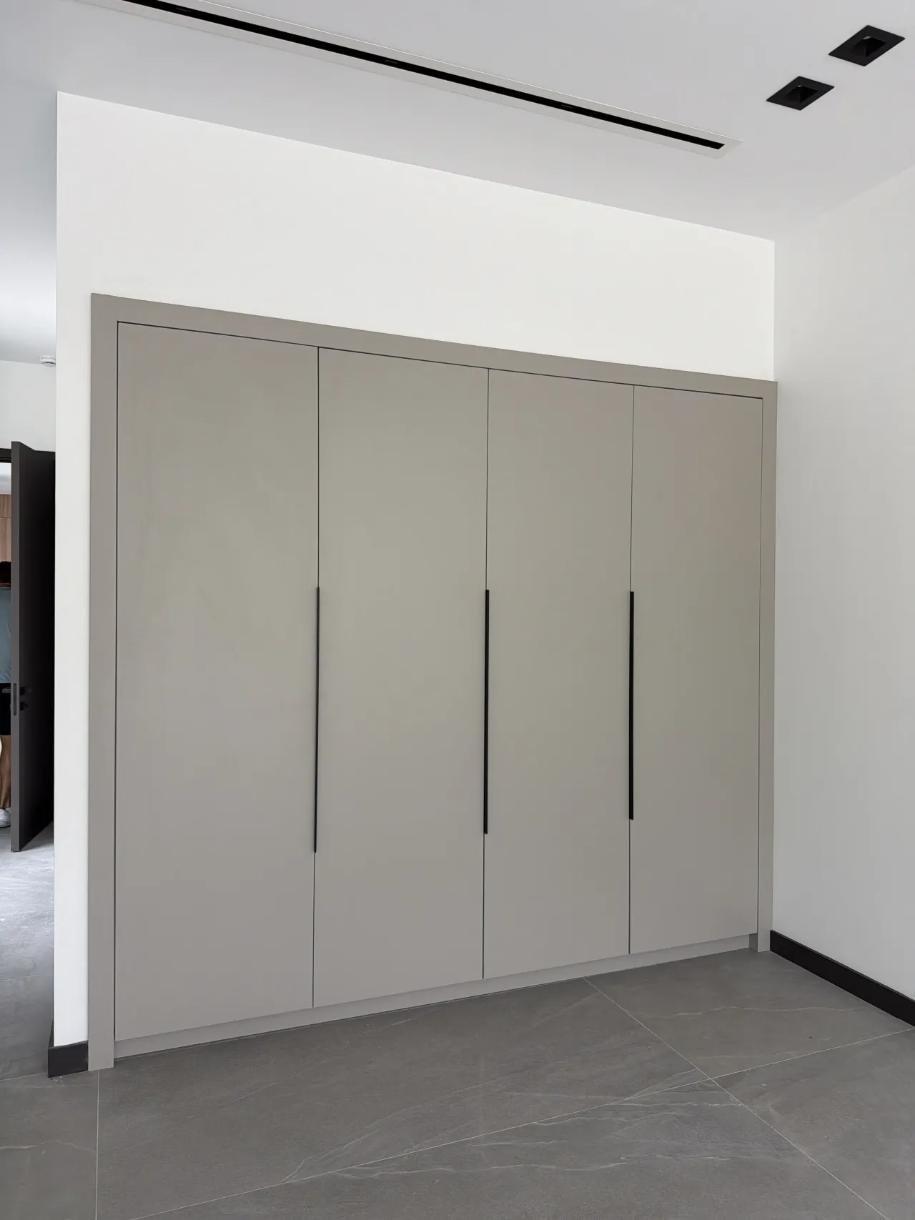 Closed greige four-door wardrobe at an angle with black bar handles and a dark door frame visible to the side