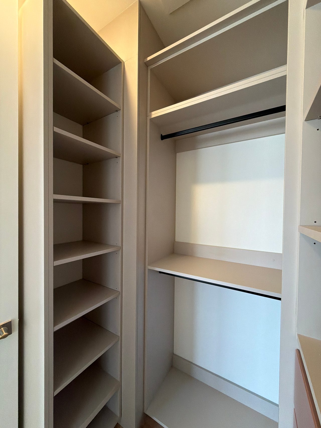 Closet corner with a tall open shelf tower at left and two stacked black hanging rods with a shelf between them, greige panels