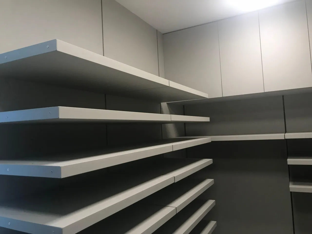 Closet corner with white floating shelves on dark gray walls, empty, and white flush-front upper cabinet doors above the shelf runs