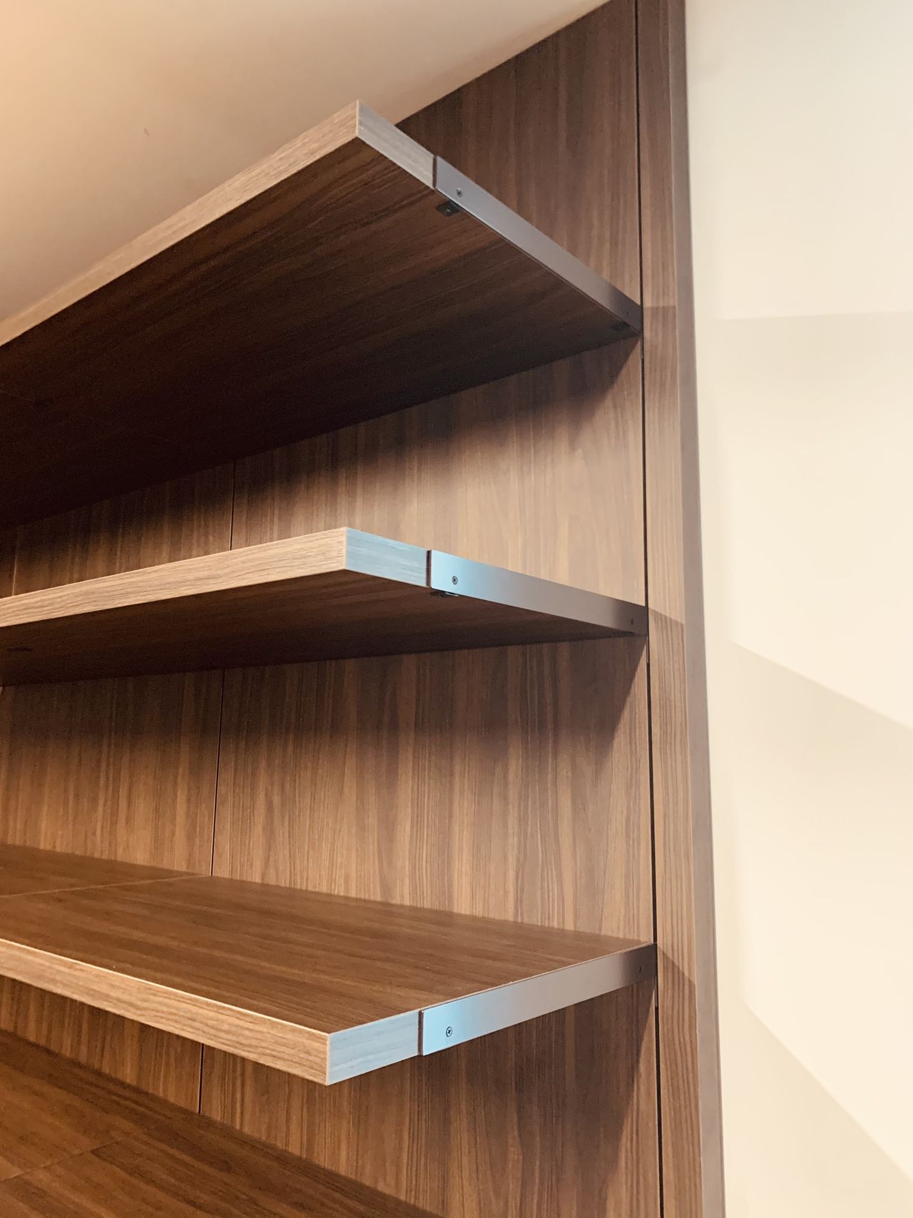 Three dark wood floating shelves with visible metal shelf-pin brackets against a dark wood-paneled wall