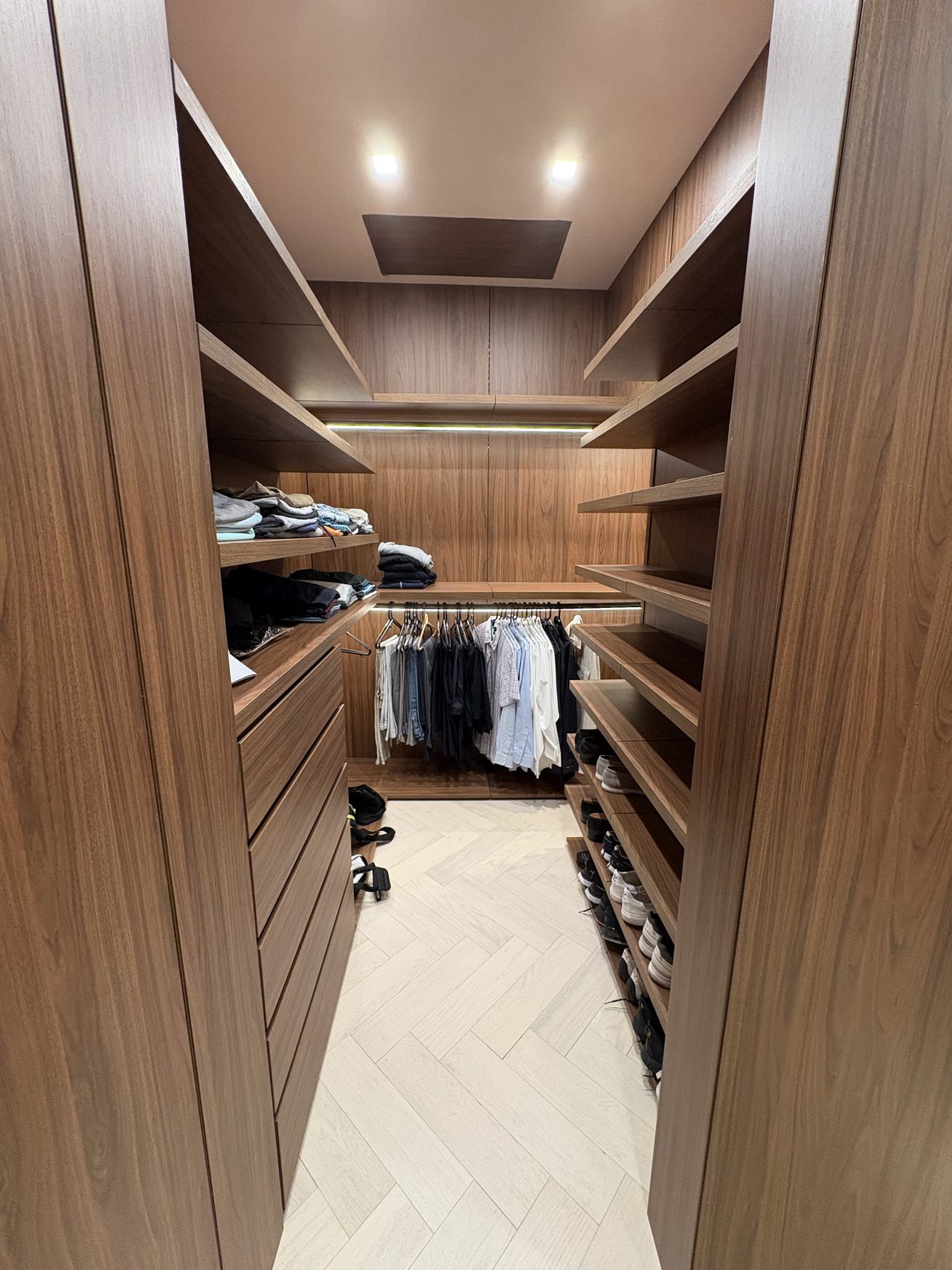 Dark wood-grain melamine closet with a drawer stack, folded clothes, and hanging garments near the entry doors