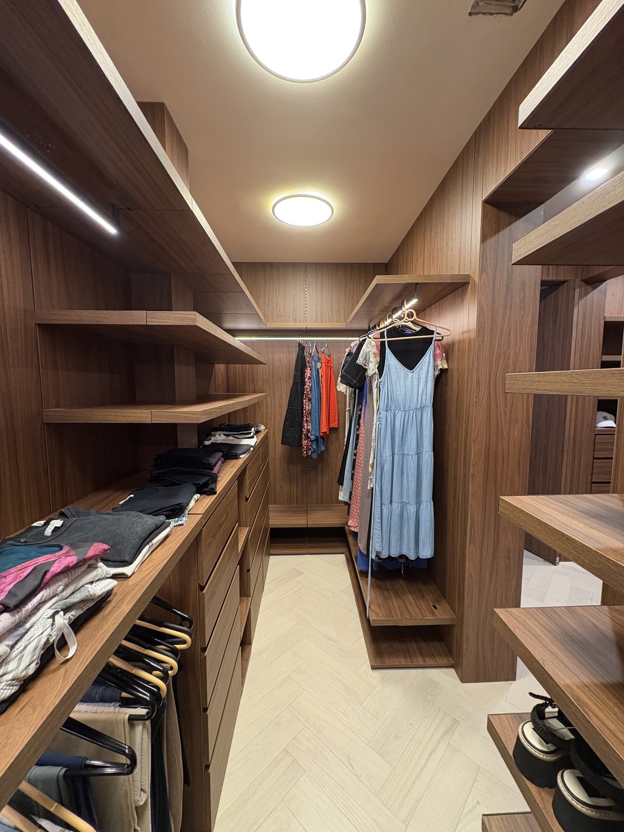 Dark wood-grain melamine closet with drawers, open shelving, and hanging jeans over a herringbone floor