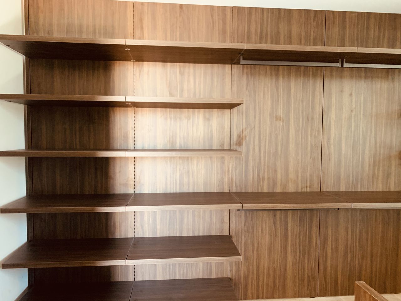 Empty dark wood open-shelf unit with a hanging rod and cabinetry, no items installed yet