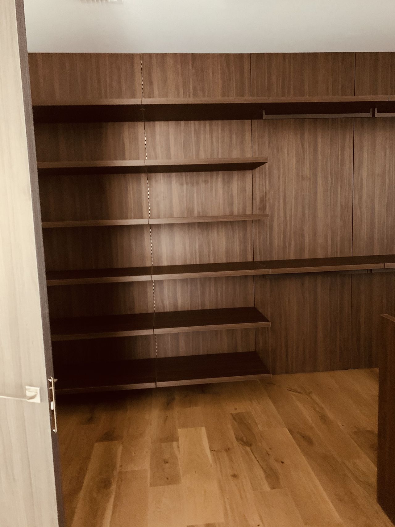 Dark wood open shelving along a wall beside a hinged door, empty shelves, light wood plank floor