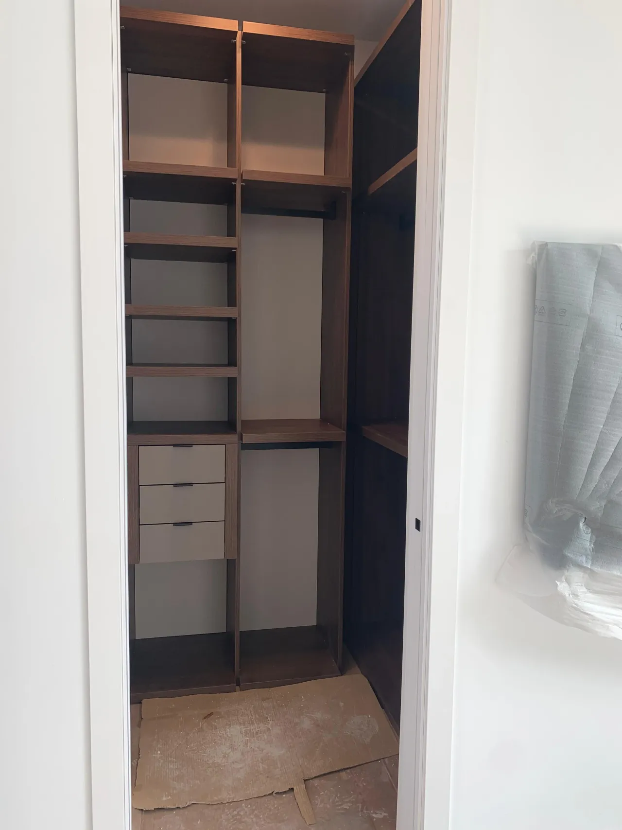 Small dark wood-toned closet interior under construction, with open shelving, a hanging area, and a taupe drawer stack