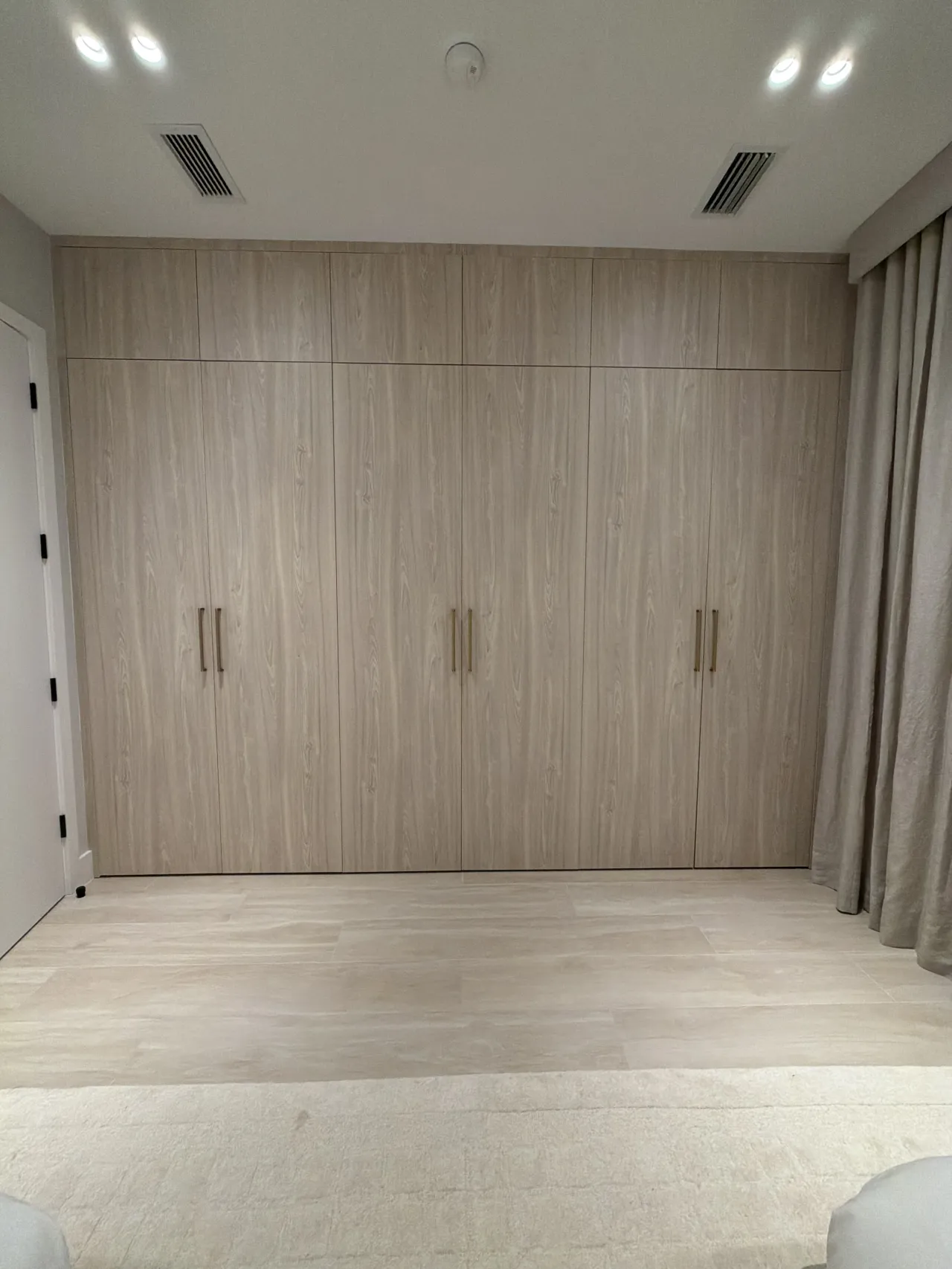 Driftwood-tone melamine wardrobe with gold-tone bar handles beside a curtained window