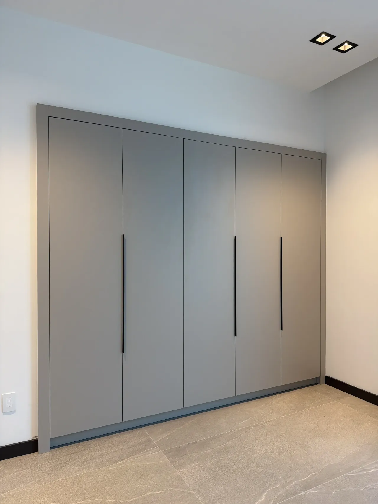Five-door gray flat-panel wardrobe wall with vertical black pull handles on a taupe stone-look tile floor