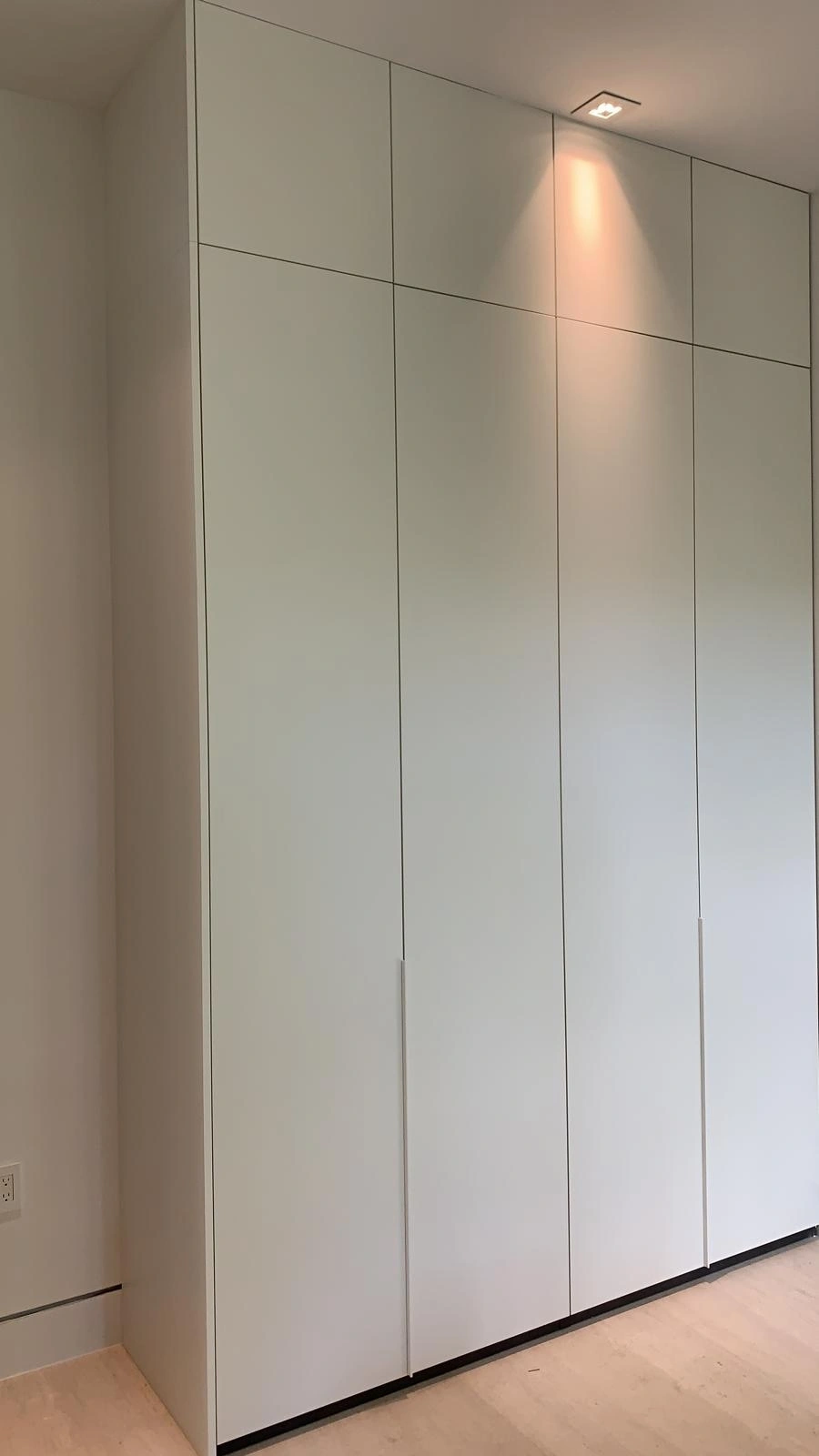 Floor-to-ceiling white closet doors with upper transom panels and slim recessed vertical pulls, set flush to a plain wall, light wood floor
