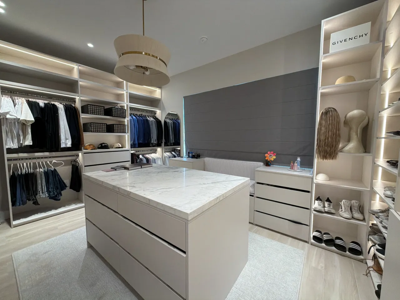 Closet with hanging clothes rods on one side and a shoe/hat shelving unit on the other around a stone island