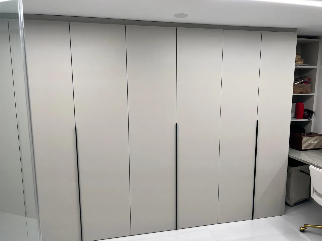 Light gray floor-to-ceiling wardrobe wall with vertical black handles, storage nook with baskets visible on the right beside it