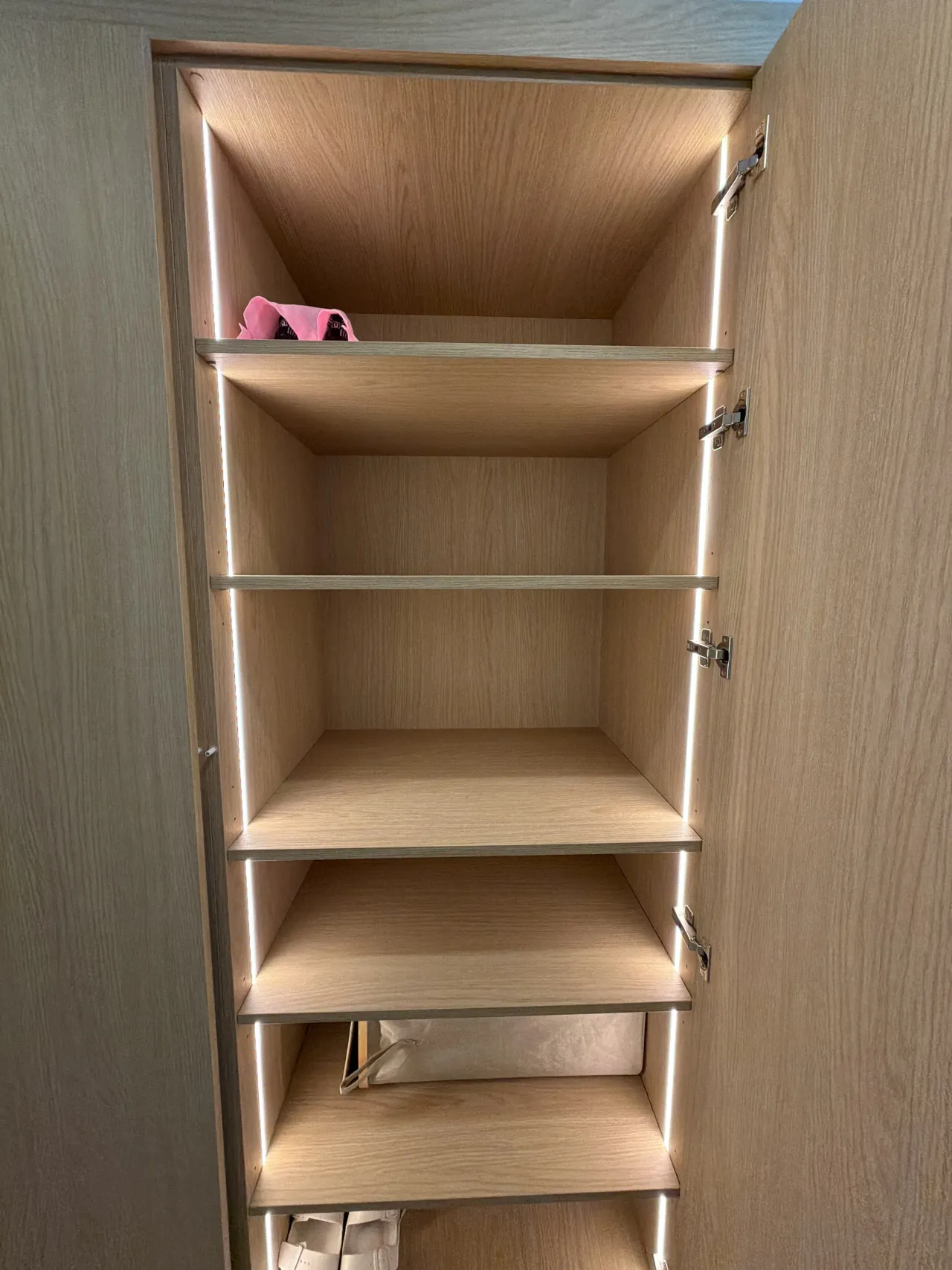 Light wood-grain melamine closet shelving with LED edge lighting, mostly empty shelves with one bag visible