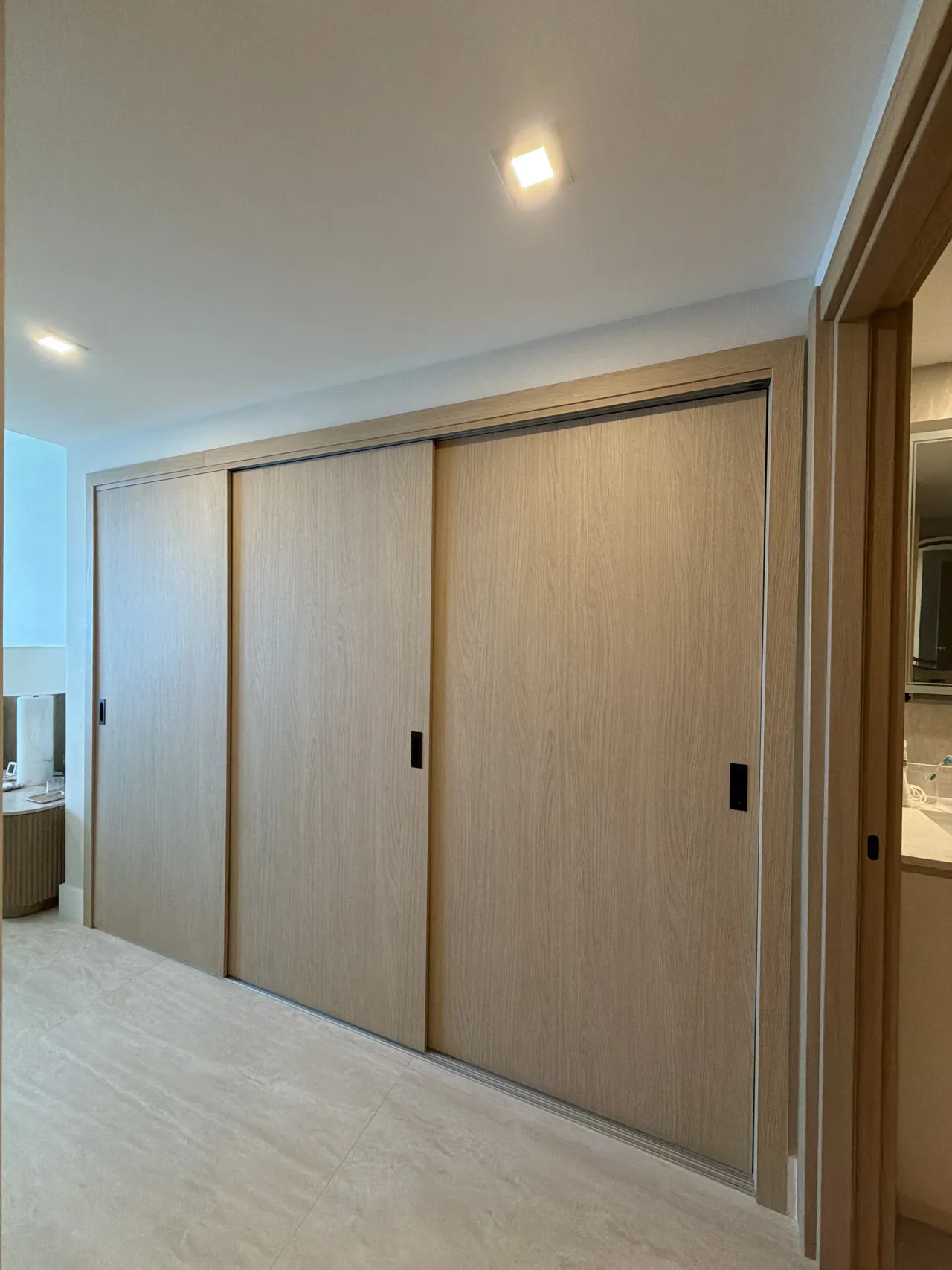 Light wood-grain melamine sliding closet doors, three panels with black tab pulls, light stone tile floor