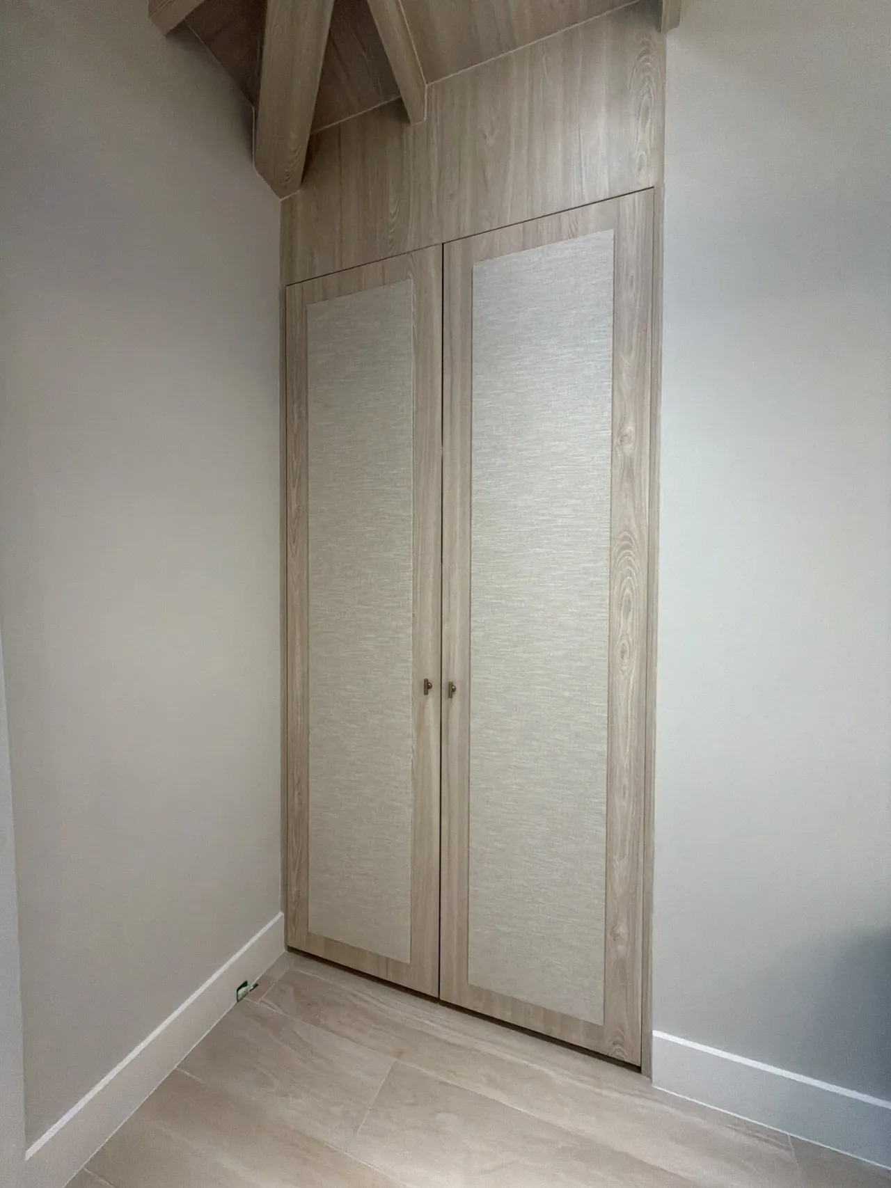 Light wood-grain melamine wardrobe with a pair of doors featuring fabric-textured insert panels and simple pull knobs