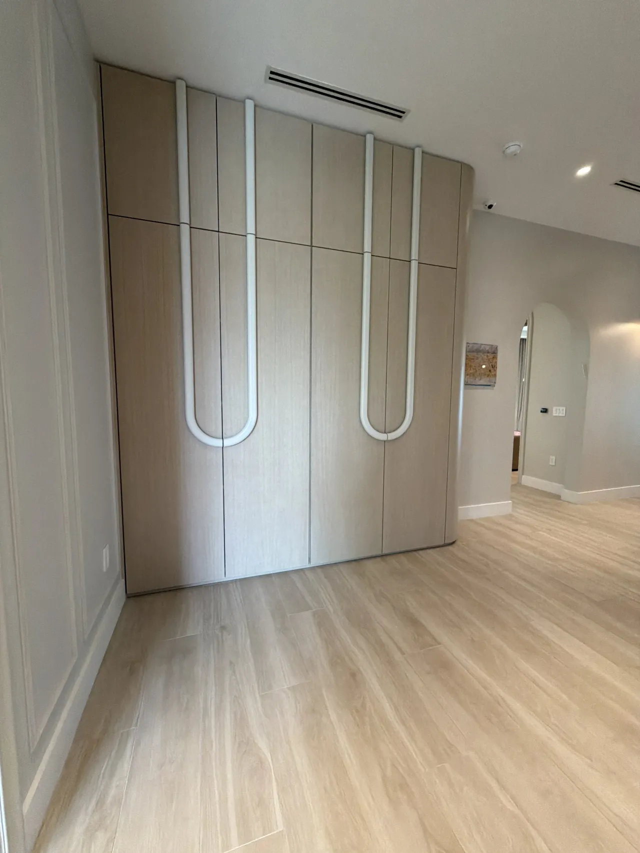 Light wood-grain melamine wardrobe wall with tall doors featuring rounded white U-shaped pull handles, on a wood-look floor
