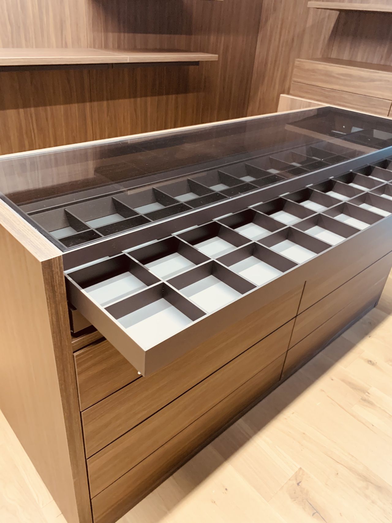 Open glass-top drawer insert with divided compartments pulled out from a dark wood closet island