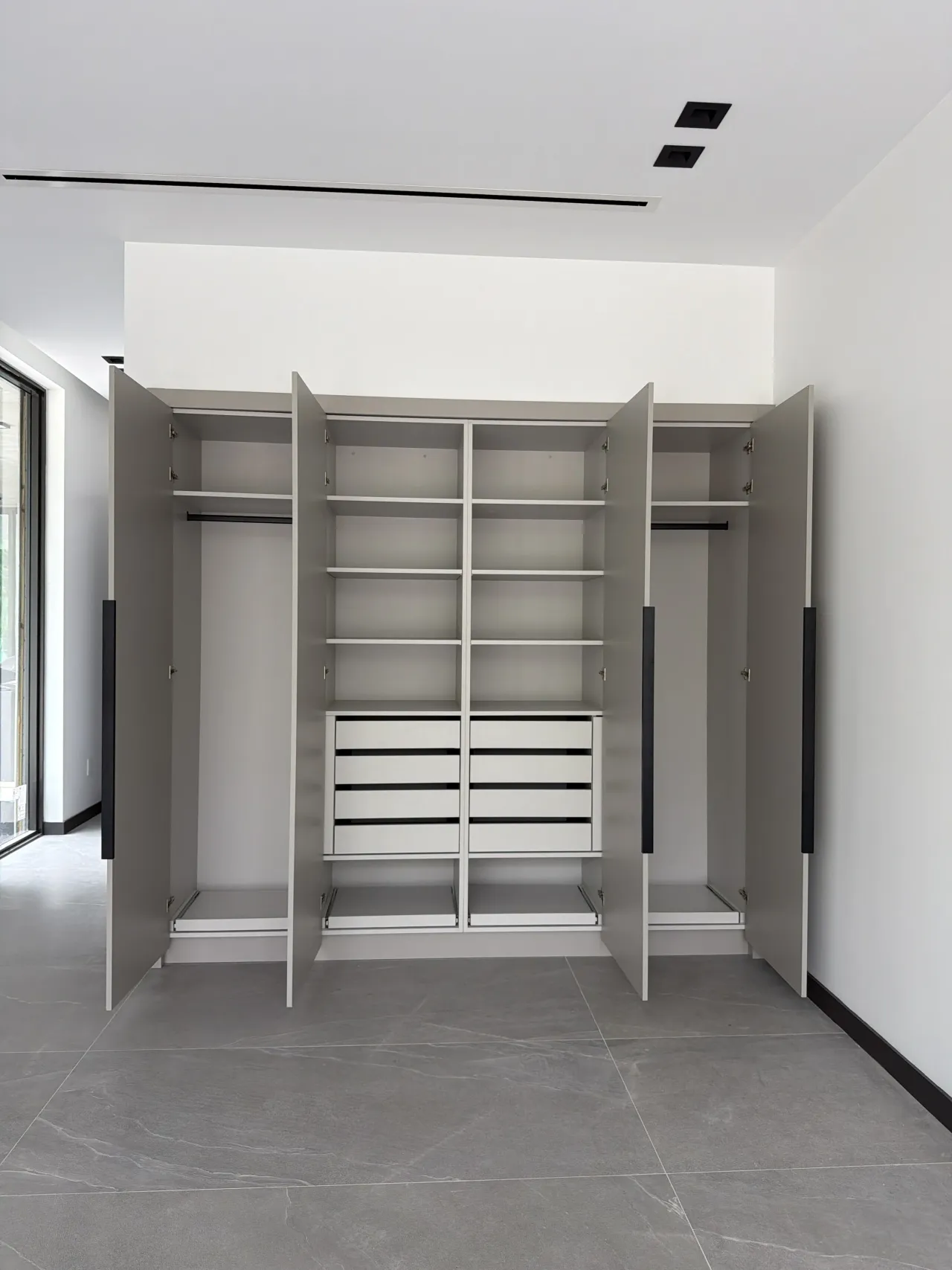 Open greige four-door wardrobe interior with hanging rods, adjustable shelves, and a center white drawer stack