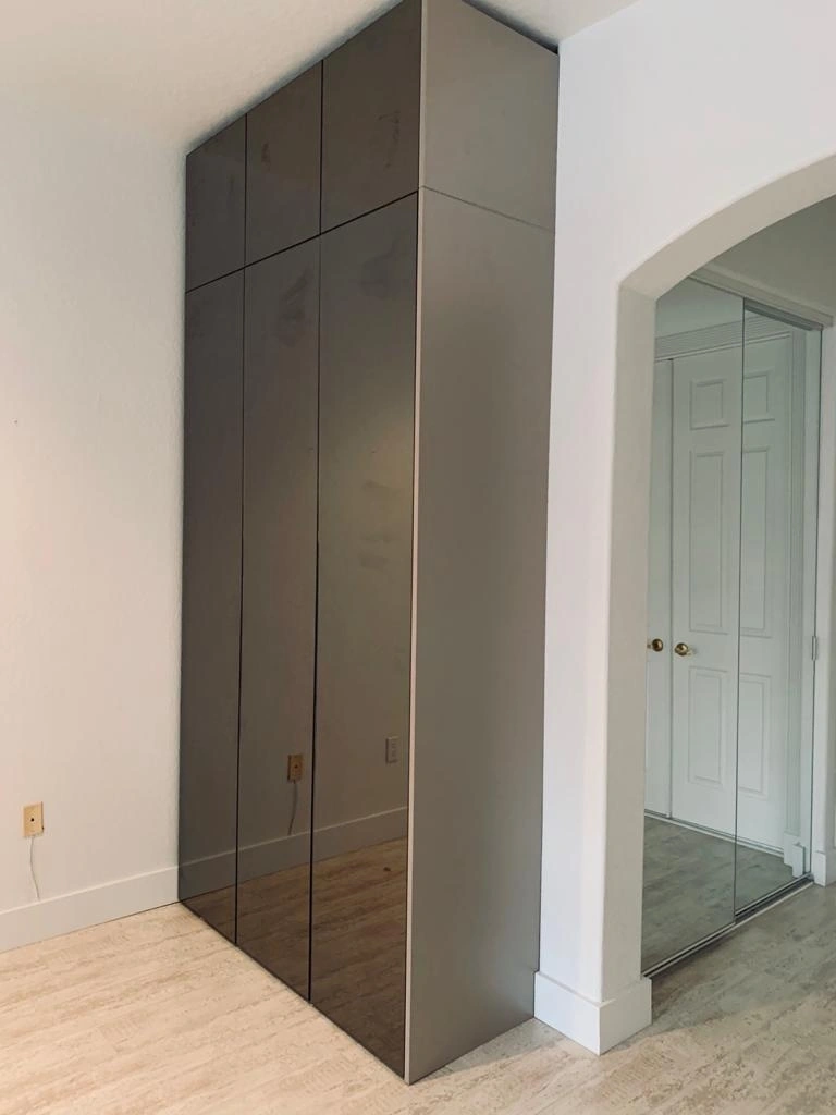 Tall taupe wardrobe with dark tinted mirror door fronts and no visible handles, beside an arched opening showing a white paneled door and mirrored closet