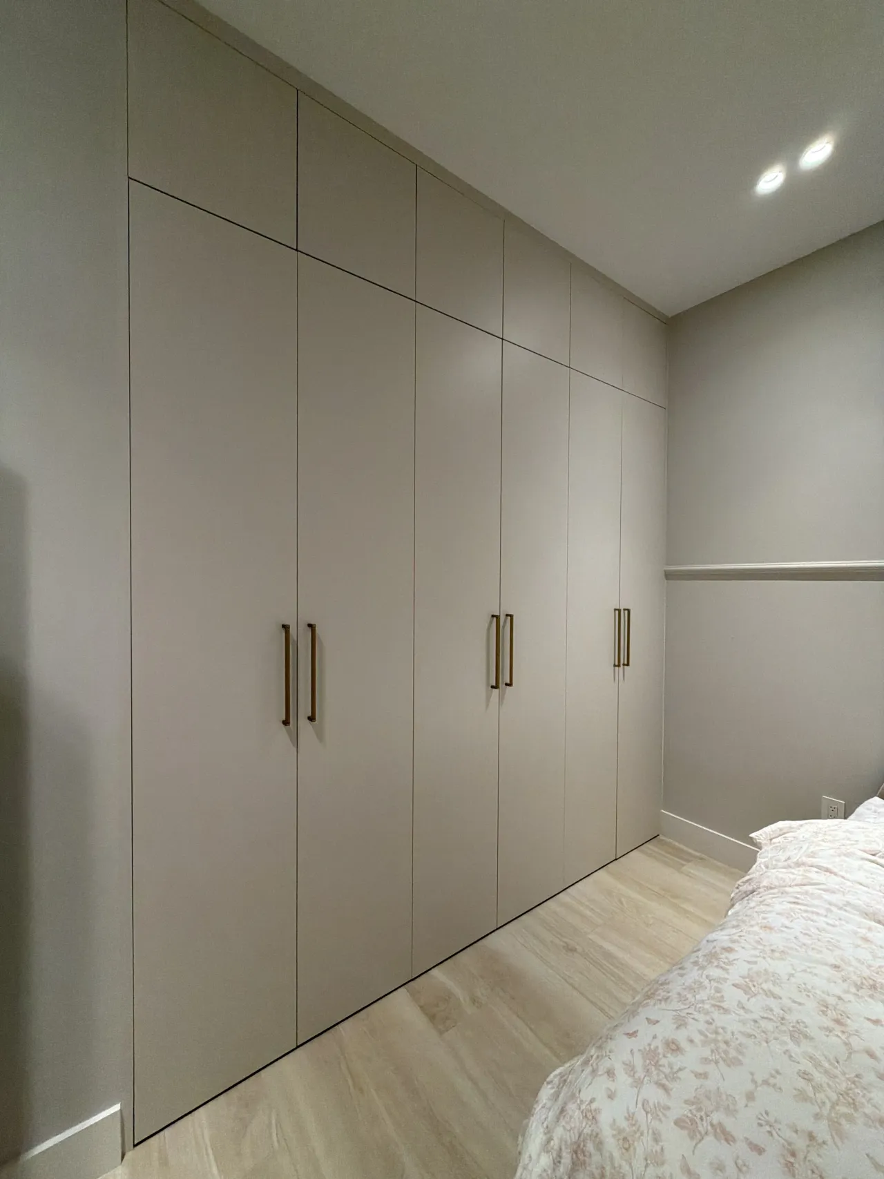 Taupe floor-to-ceiling wardrobe with gold-tone bar pulls in a bedroom with a floral bedspread