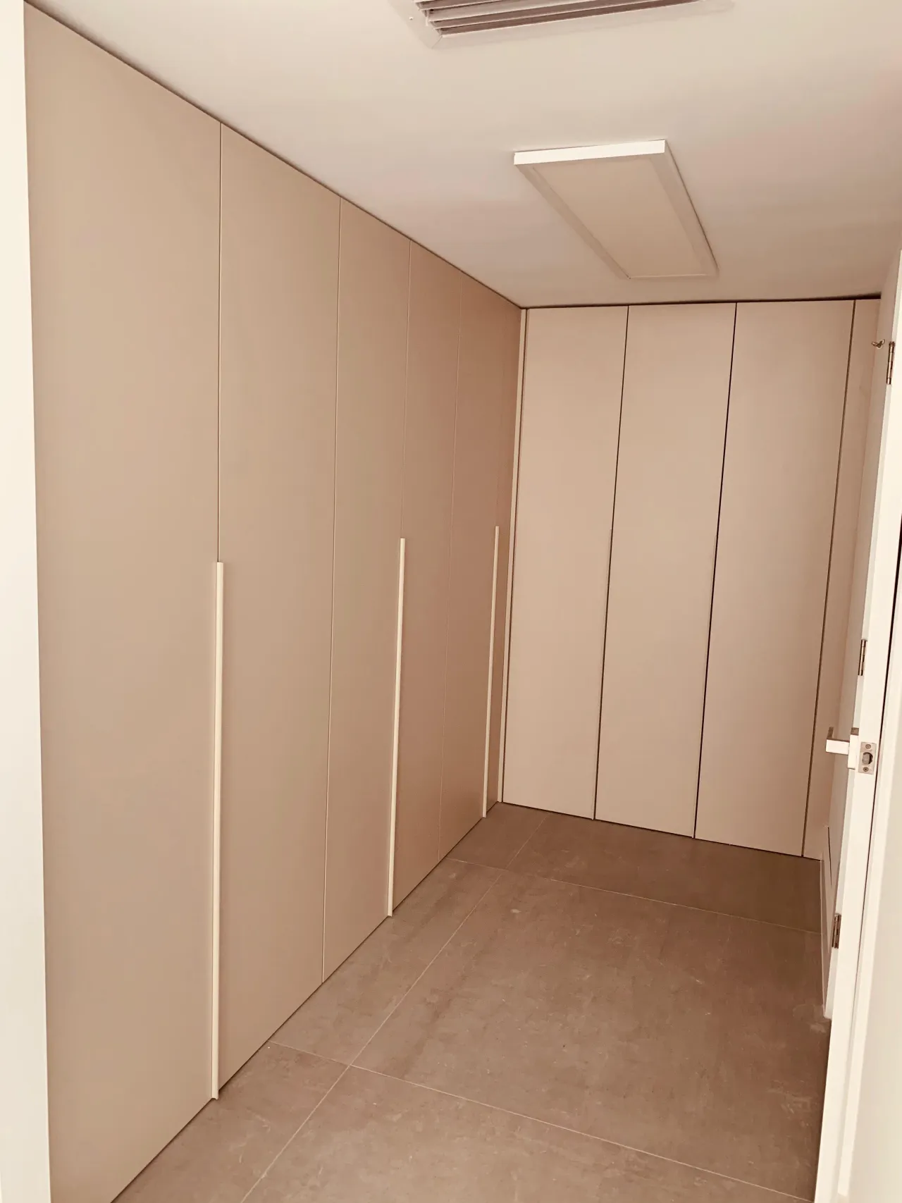 Taupe floor-to-ceiling wardrobe with long vertical handles running down a hallway, gray tile floor
