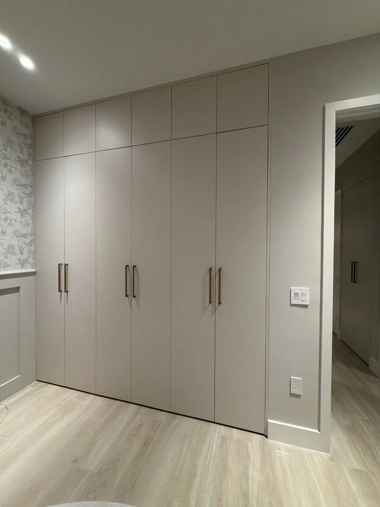 Taupe wardrobe wall with gold-tone bar pulls next to a bedroom door, wood-look floor