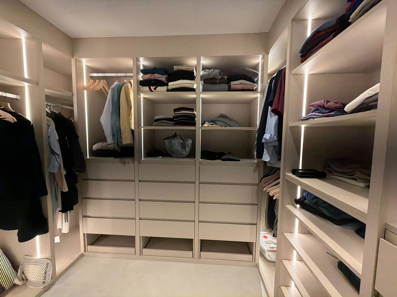 Gray melamine closet with three LED-lit drawer towers under open shelving, hanging rails on both side walls, and open cubbies beneath