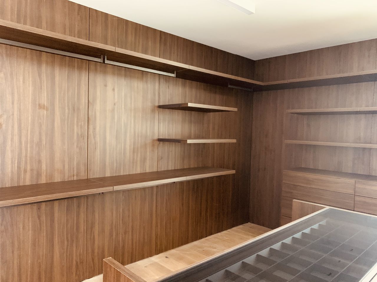 Unfinished dark wood closet corner with open shelving and a staircase glimpsed at the bottom of frame