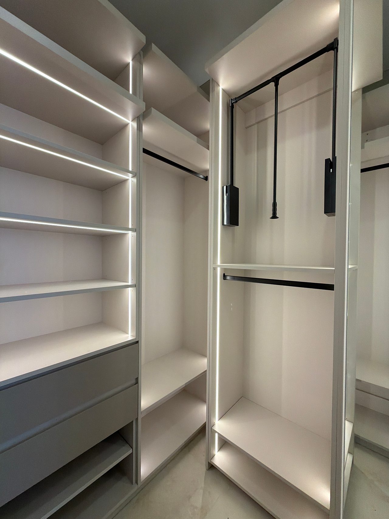 Walk-in closet with LED-lit shelves and drawers at left and a tall unit at right holding a pull-down rod above a fixed hanging rod