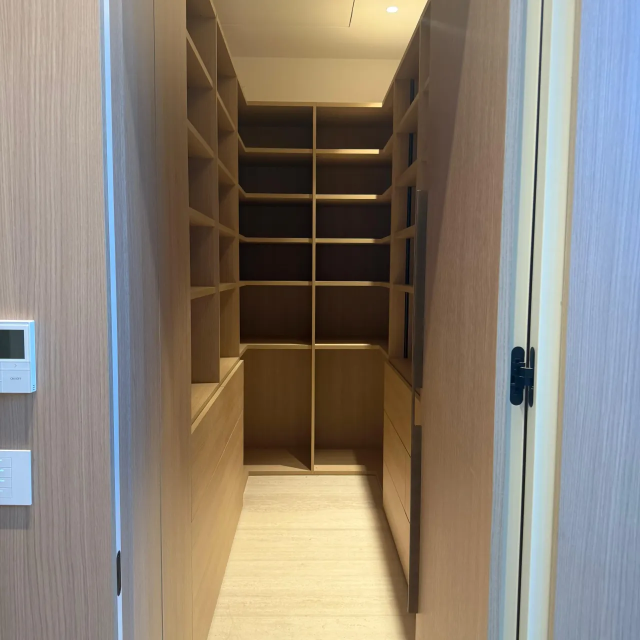 Narrow walk-in closet with light wood-grain open shelving and cubbies, a low drawer bank, and integrated LED lighting under the shelves