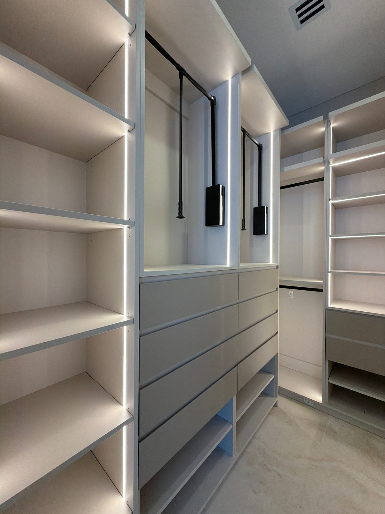 Walk-in closet with two pull-down hanging rods over a bank of drawer fronts, LED-lit open shelving at left and a stone-look tile floor