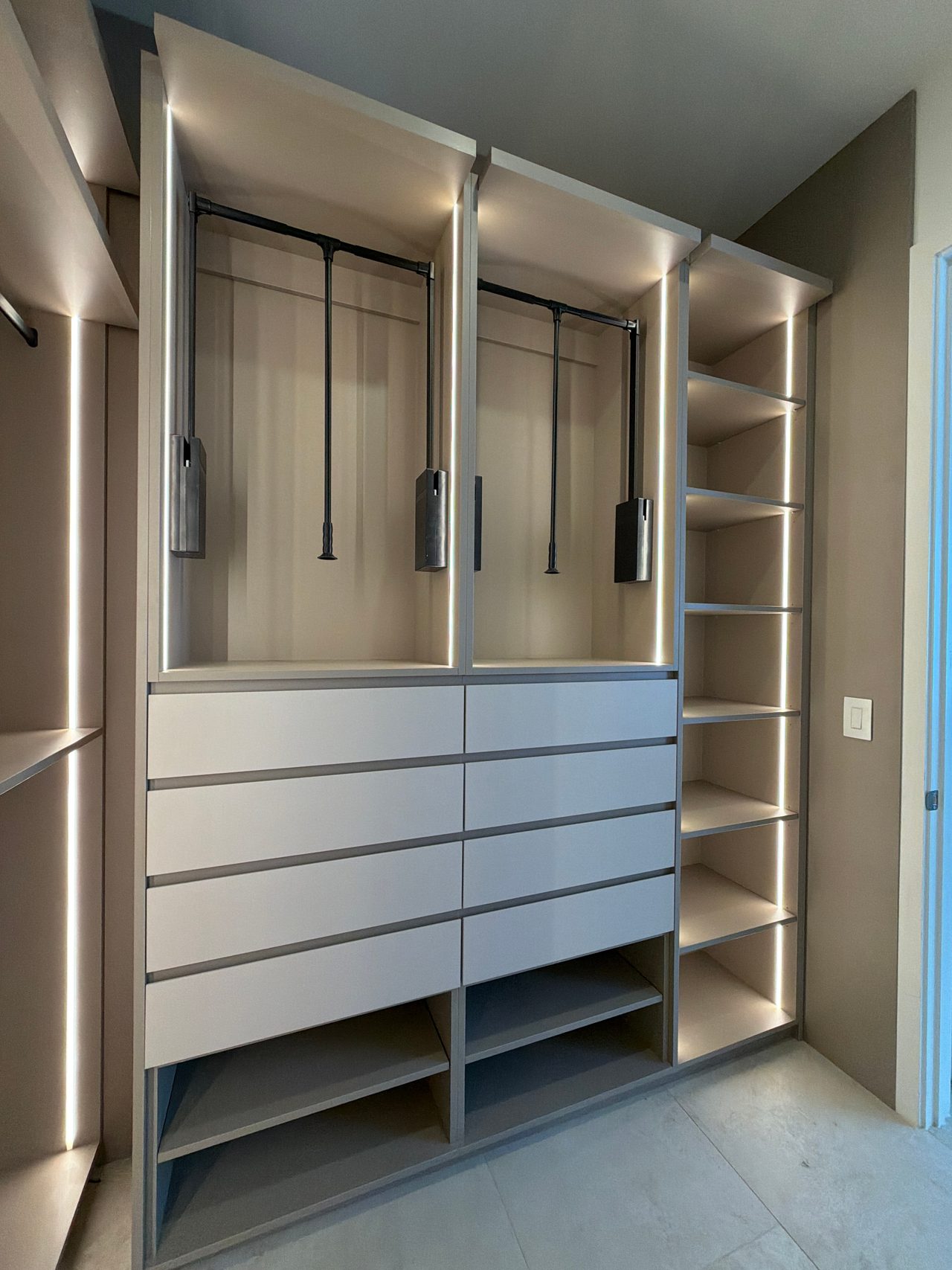 Walk-in closet with two pull-down hanging rods, LED-lit shelving, a bank of white drawer fronts and a tall open shelf column at right
