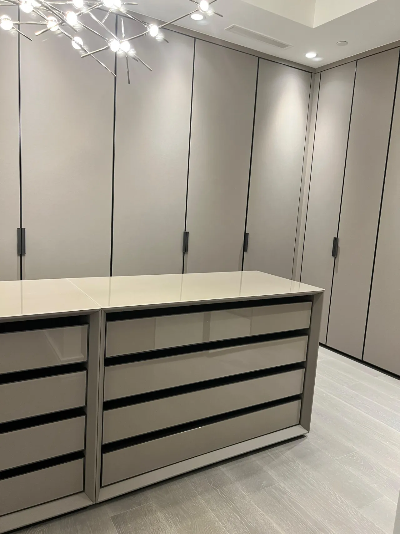 Walk-in closet with taupe-gray floor-to-ceiling wardrobe doors, a central drawer island with a white top, and a starburst chandelier overhead
