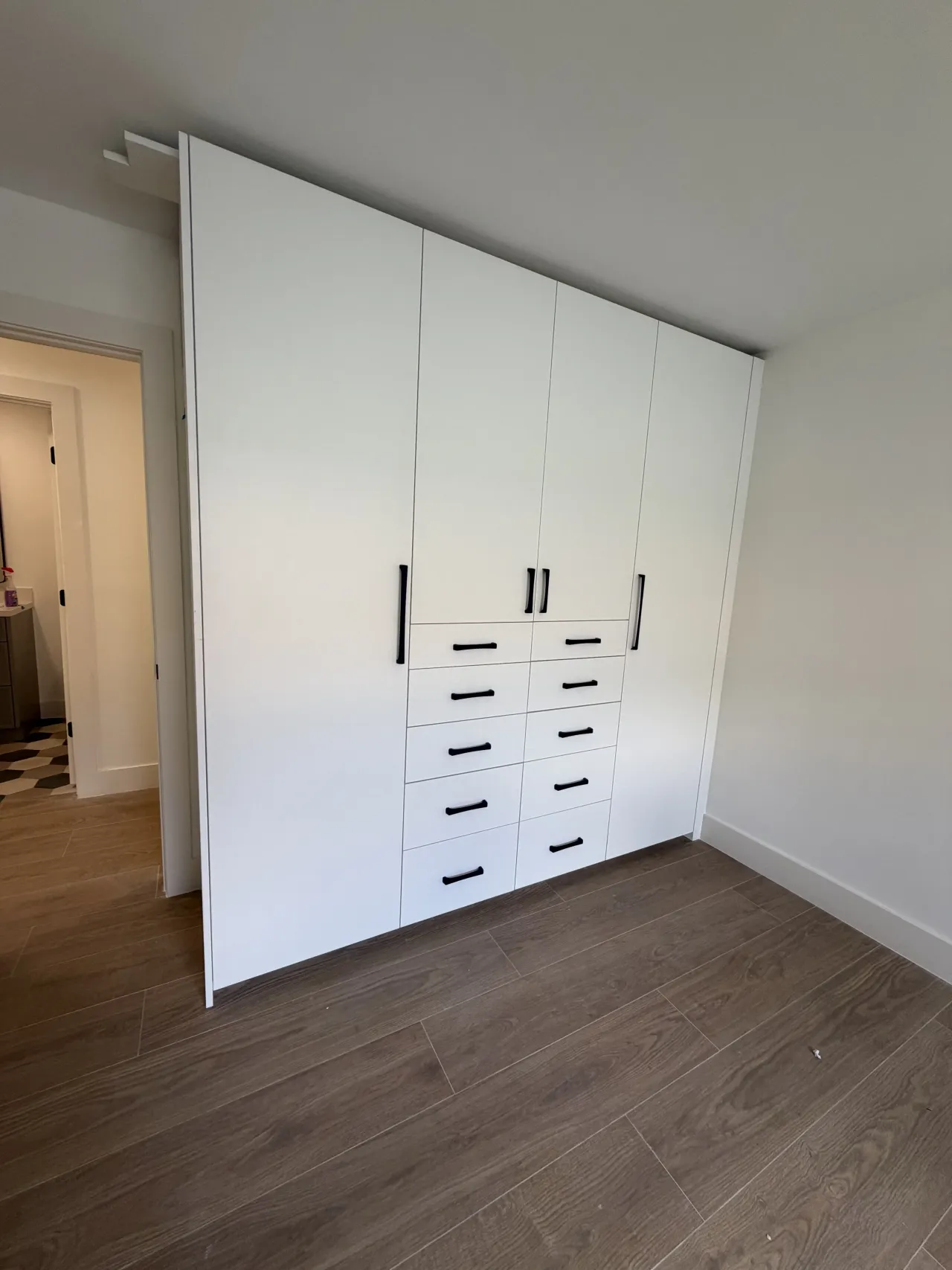 White wardrobe with double column drawers and black pulls, showing full wardrobe height and a doorway to the left