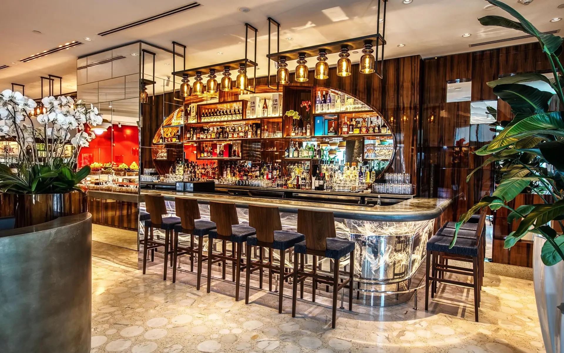 Restaurant bar with dark wood-grain paneling, an illuminated back-bar display, and gold-tone pendant lights
