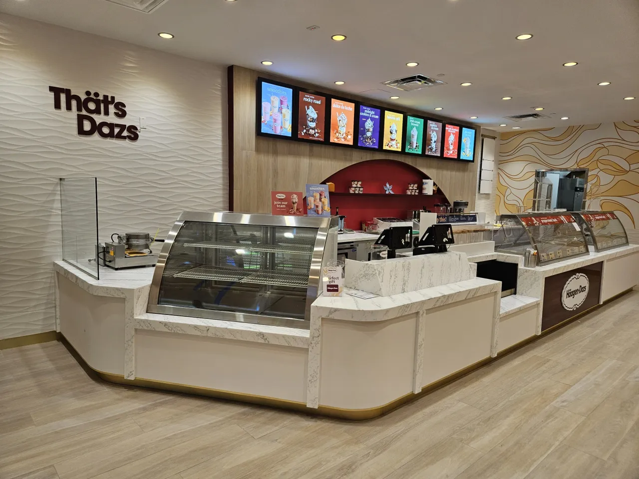 Curved white veined stone ice cream shop counter with stainless display cases and menu boards, on a light wood-look tile floor