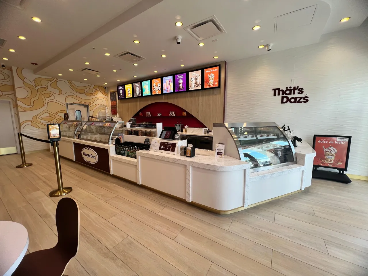 Finished ice cream counter with veined stone top, white and dark red fronts, curved glass display case, gold-tone stanchion post with rope