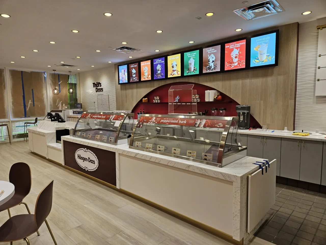 Ice cream shop interior with straight-run veined stone display counters, illuminated menu screens overhead, wood-grain wall and an arched red niche
