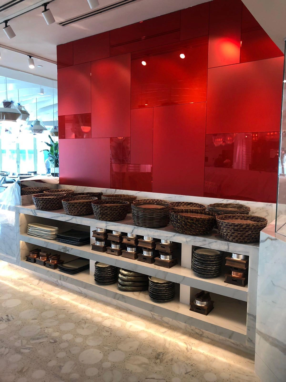 Red glossy glass feature wall panel system above open shelving holding stacked plates, bowls, and dining ware