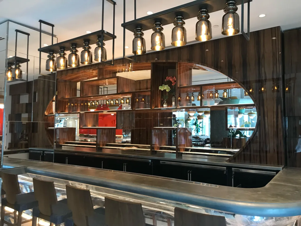 Restaurant bar with dark wood millwork, an oval mirrored accent panel, hanging bottle pendant lights, upholstered barstools