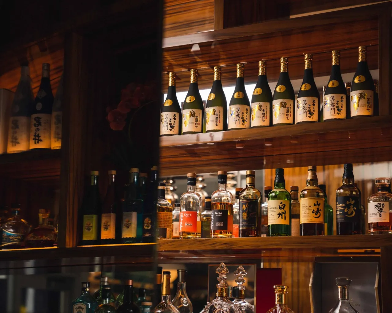 Restaurant bar shelving stocked with spirit bottles against a dark wood-paneled backdrop
