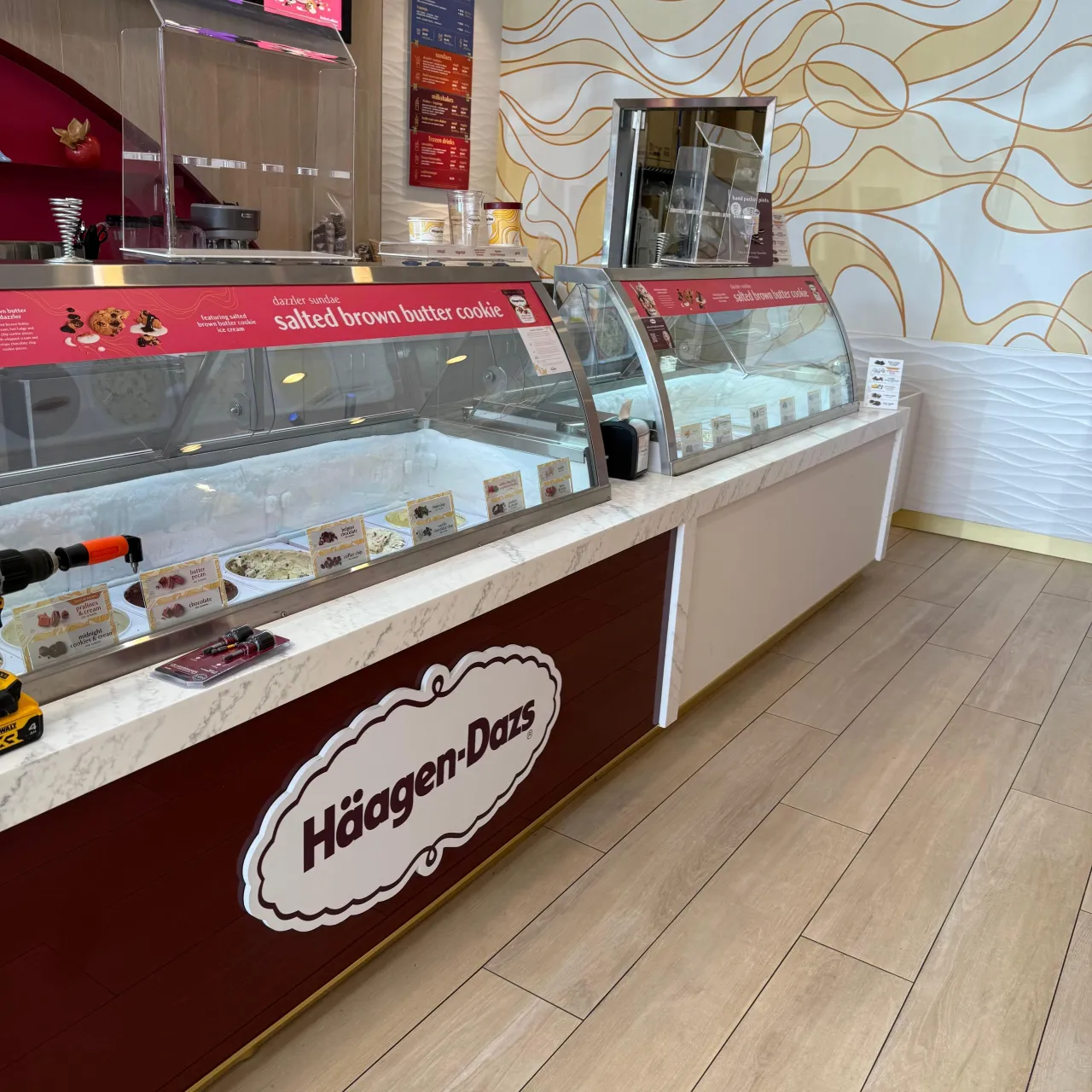 Veined stone-topped ice cream display counter with a dark maroon front panel and curved glass display case, light wood floor