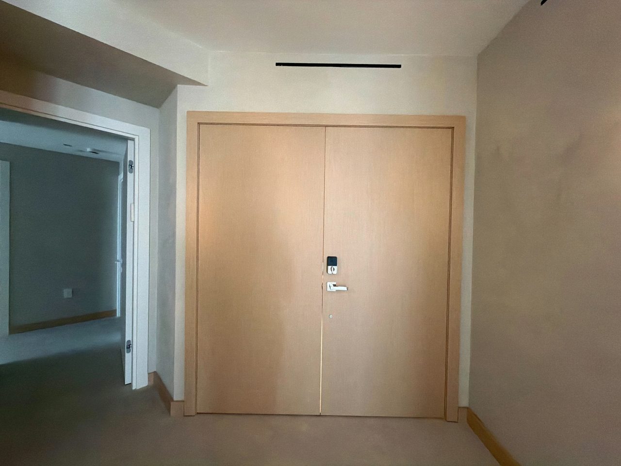 Tall custom-stained wood veneer double door with a keypad lock and lever handle, set in matching wood casing beside an open hallway doorway