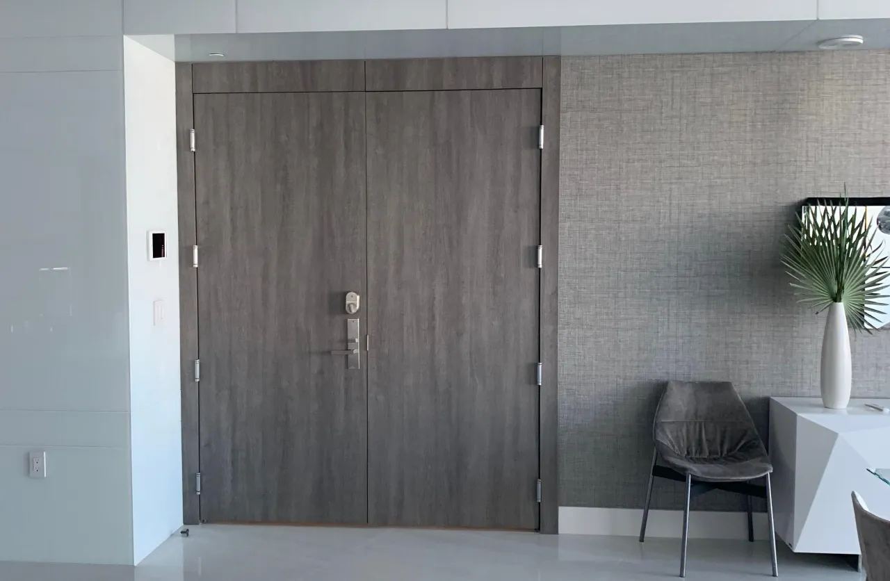 Dark wood-grain double entry door with a lever handle and deadbolt, set into a gray wallpapered wall, stone-look floor